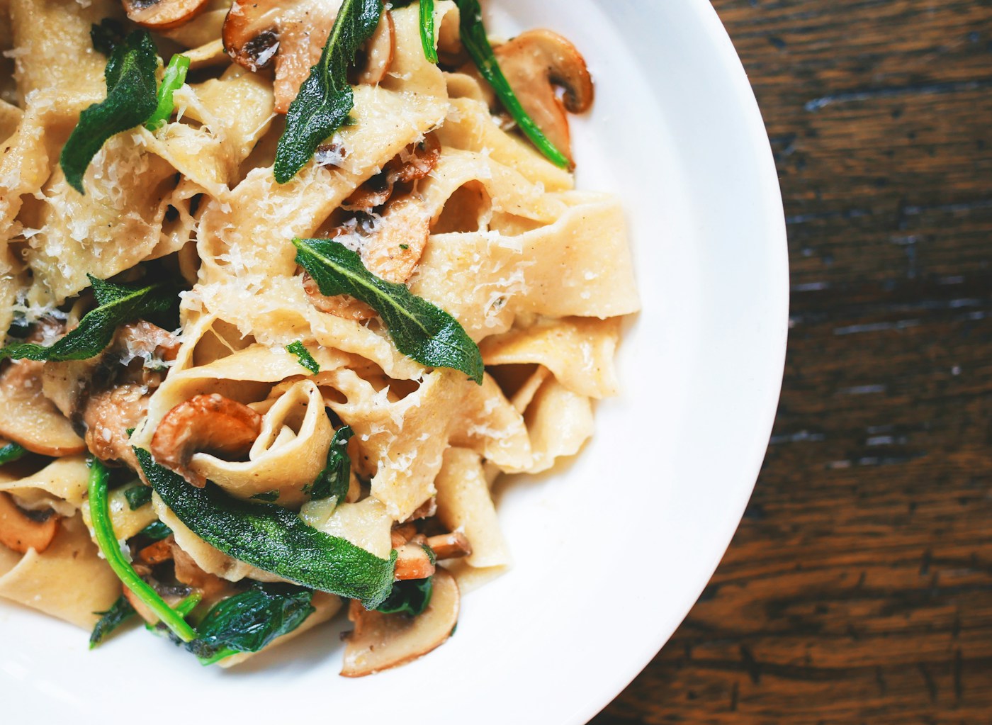 Main course ribbon pasta tossed with cooked mushrooms, wilted greens, and grated cheese