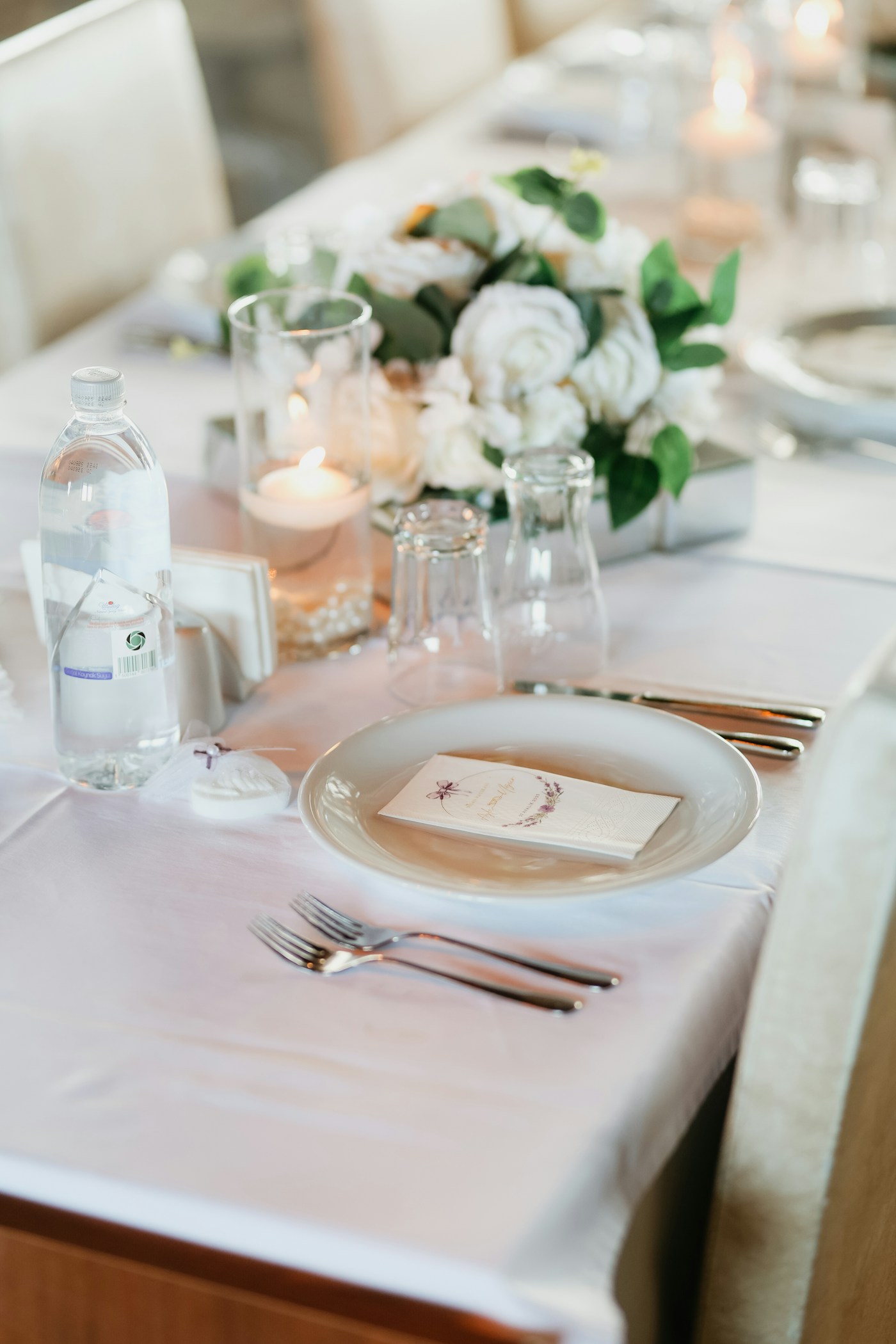 Candlelit banquet table set with white tablecloth, fine glassware, dinner plates, and white rose floral centerpieces